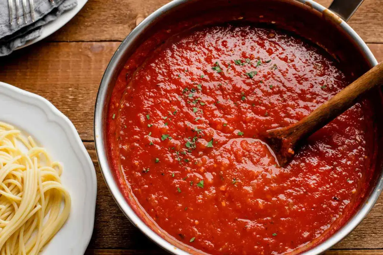 Ein Topf mit köstlichem Sugo di Pomodoro, bereit, über frische Spaghetti gegossen zu werden. Ein Holzlöffel rührt in der rubinroten Sauce.