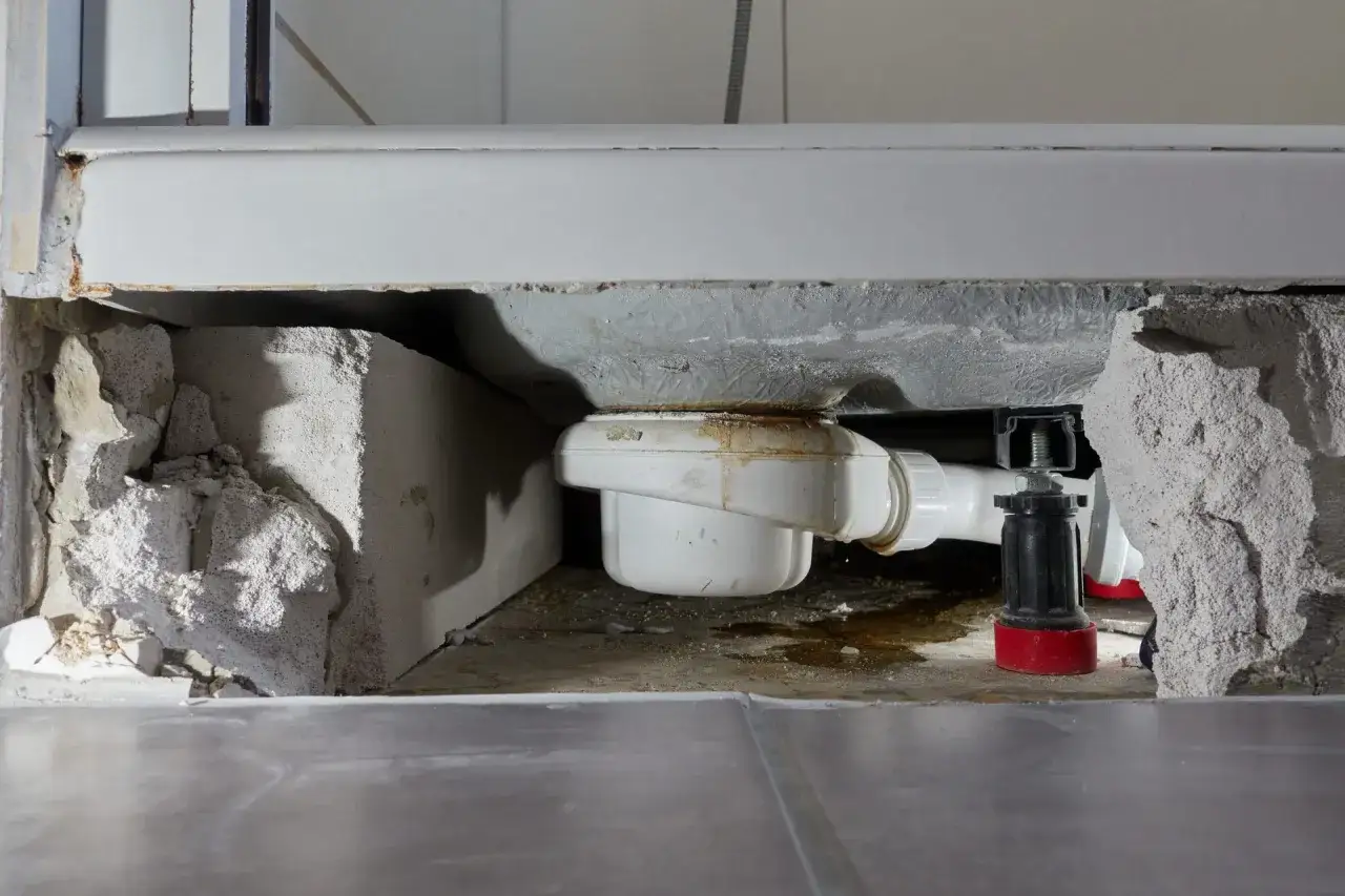 Undichte Dusche verursacht unverschuldeten Wasserschaden in Eigentumswohnung. Sichtbar sind abgebrochene Bauteile und ein abgenutzter Abfluss.