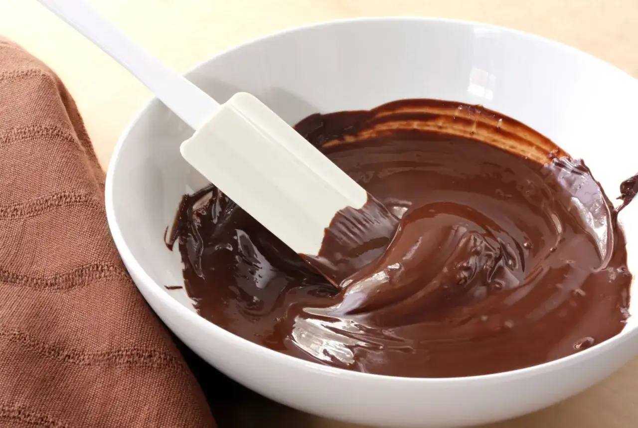 Chocolate fundido y brillante en un bol blanco, con una esp&aacute;tula removiendo. El proceso de como derretir chocolate es sencillo y delicioso.