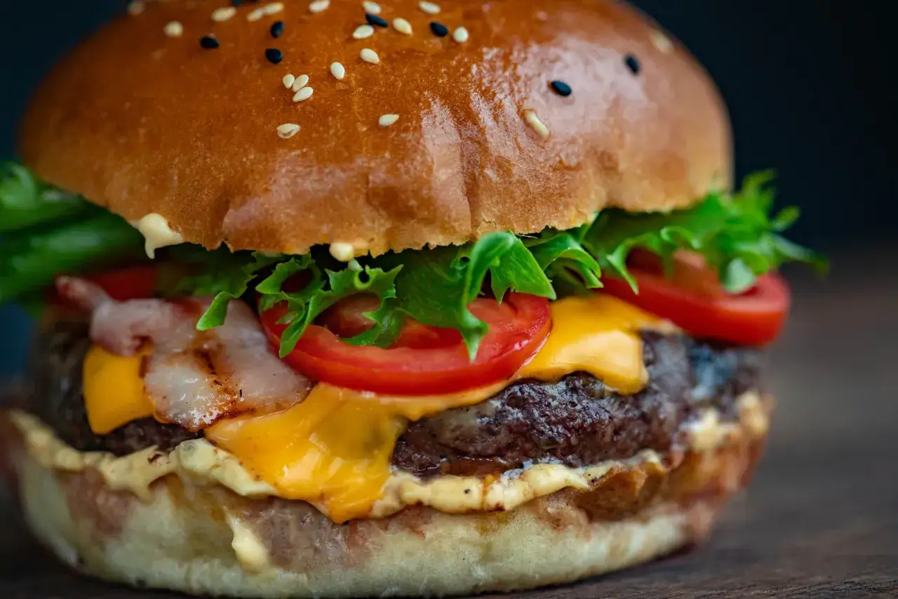 Soczysty burger z wołowiny, idealne jakie mięso na mielone, z serem, bekonem, pomidorem i sałatą w bułce z sezamem.