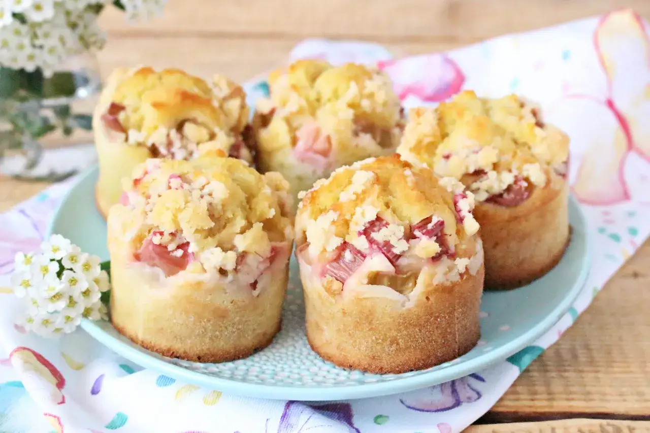 Pięć pysznych muffinek z rabarbarem, posypanych kruszonką, na talerzyku z wiosennym motywem.