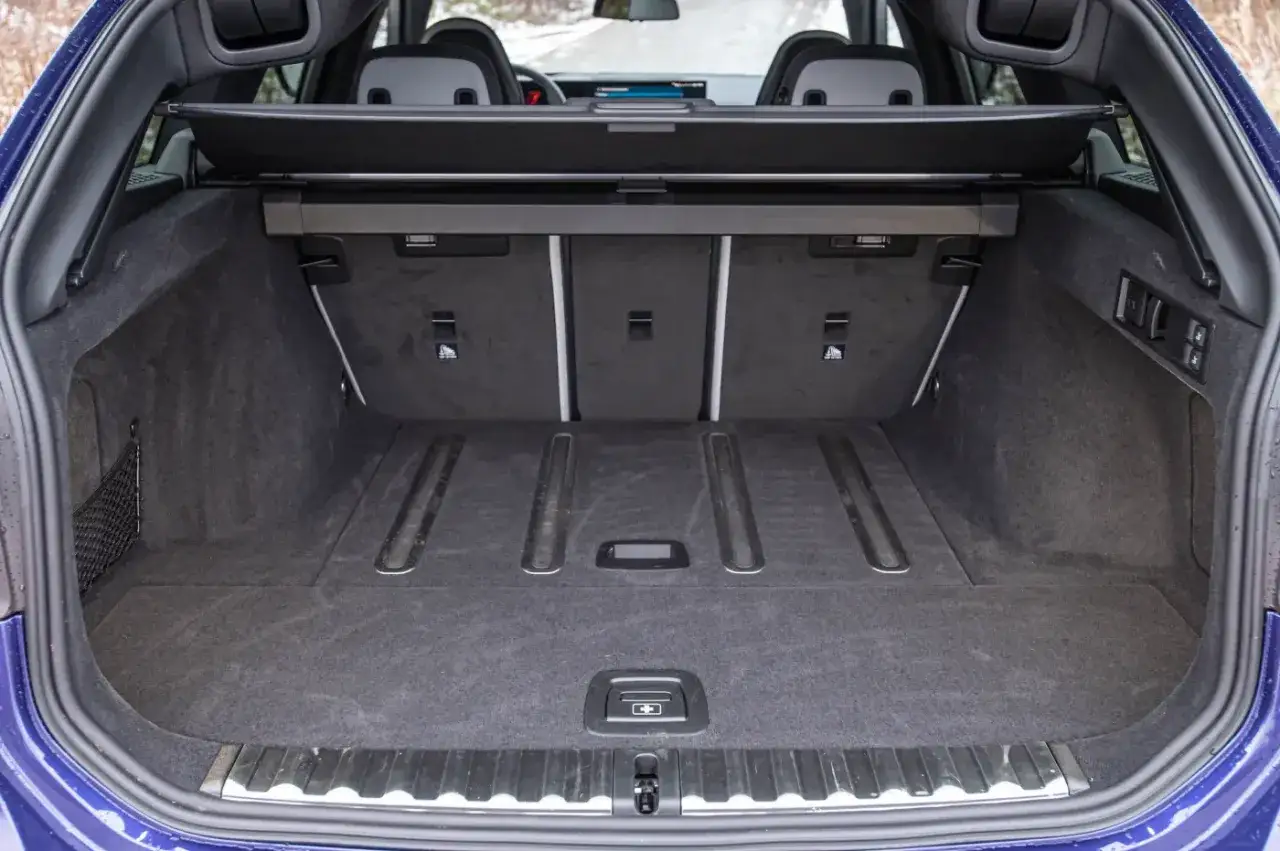 Pusty bagażnik BMW M3 Touring. Wnętrze wyłożone ciemną wykładziną, z siatką po lewej stronie i metalowymi szynami na podłodze.