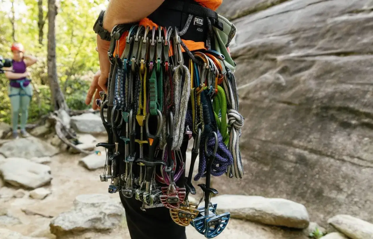 Klettergurt mit vielen Karabinern und Klemmkeilen, bereit f&uuml;r trad climbing. Eine Kletterin im Hintergrund.