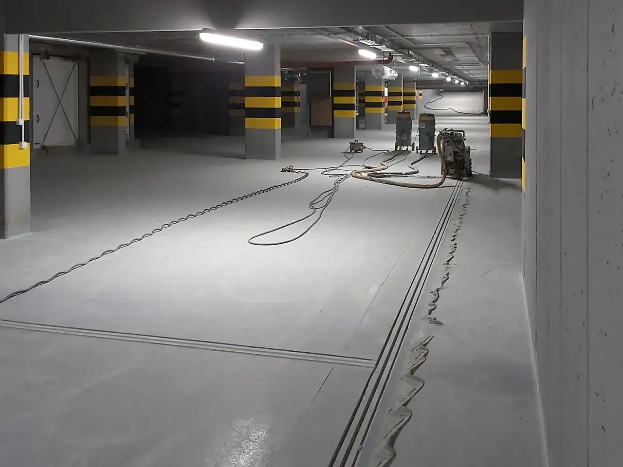 W garażu montowany jest odwodnienie liniowe. Widać maszyny i kable na betonowej posadzce.