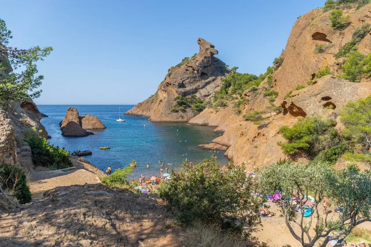 A sunny day at the calanques, with people enjoying the beach and swimming in the clear blue water. This idyllic scene evokes the feeling of camping calanques.