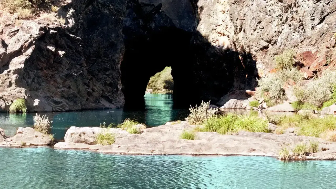 Agua turquesa fluye hacia un monte furado, una entrada natural en la roca que revela un paisaje verde.