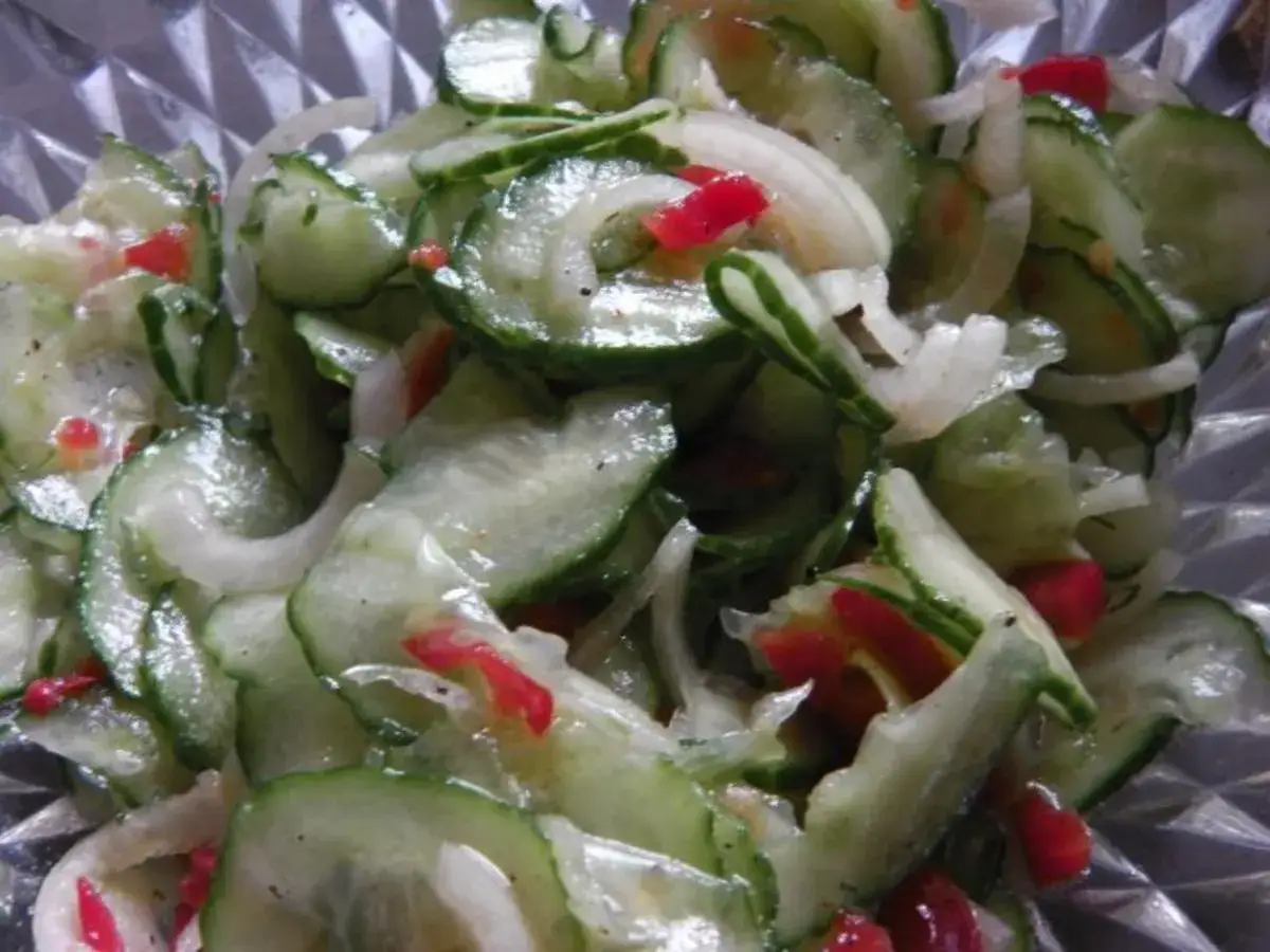 Frischer gurkensalat ohne zucker, mit Zwiebeln und roten Paprikastückchen, in einer Glasschüssel.