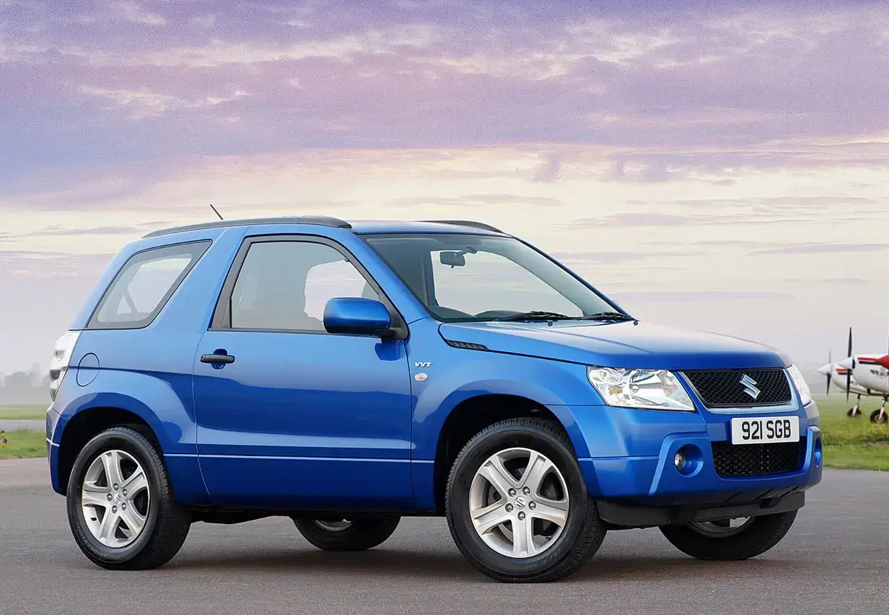 Niebieski Suzuki Grand Vitara 2005 na tle nieba z chmurami i samolotami w tle.