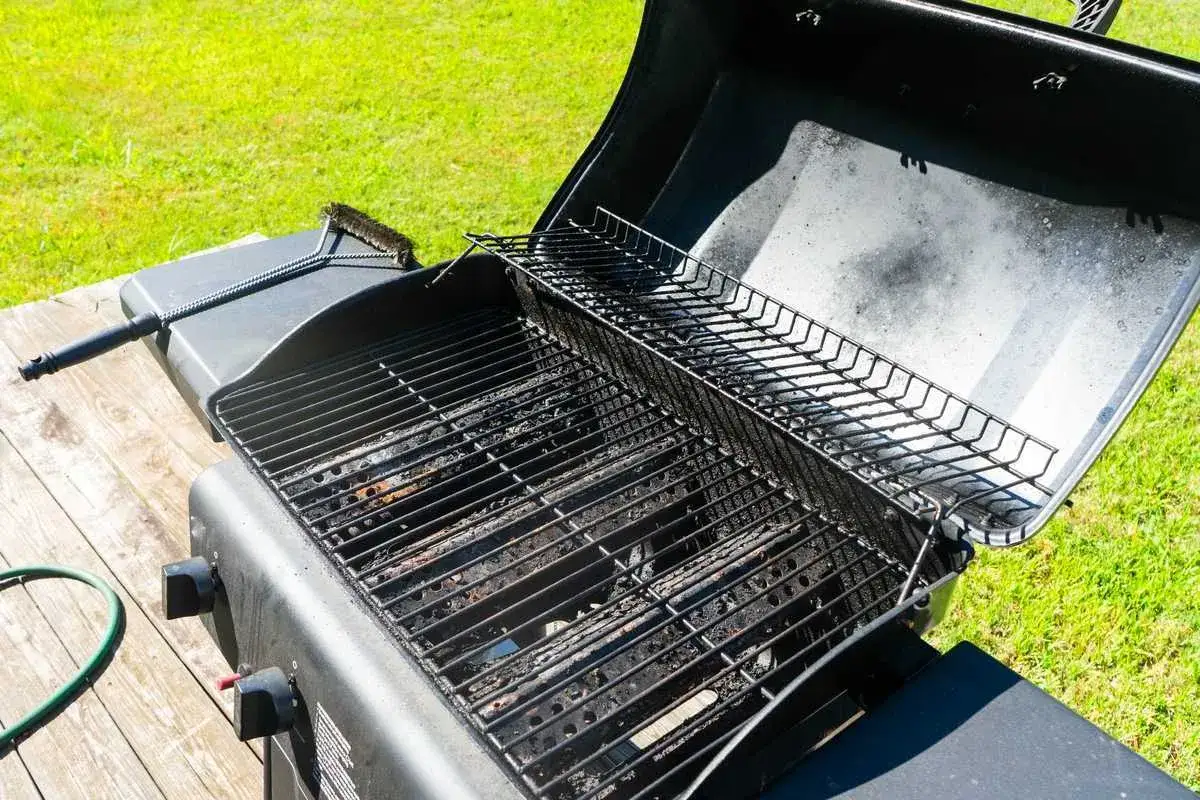Un barbecue &agrave; gaz pr&ecirc;t &agrave; nettoyer, avec une brosse &agrave; port&eacute;e de main. Les grilles sont sales, signe qu'il est temps de le faire briller pour la prochaine cuisson.
