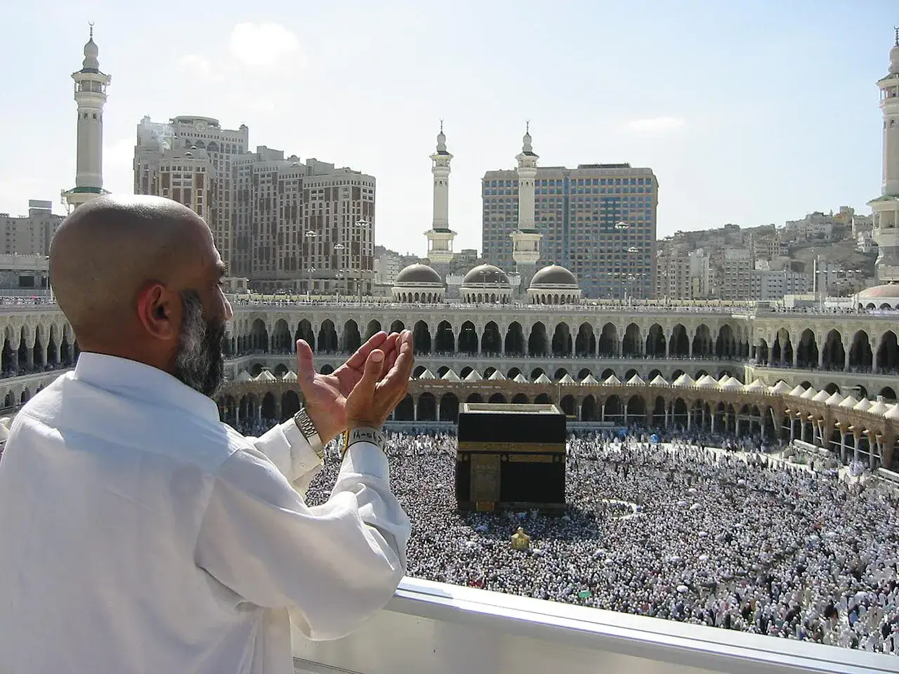 Mann betet mit erhobenen Händen vor der Kaaba in Mekka, Saudi-Arabien. Tausende Pilger umgeben das heilige Gebäude.