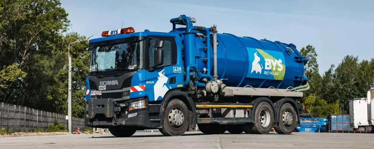 Niebieska cysterna marki Scania, gotowa do czyszczenia szamba. Logo BYŚ Recycling na burcie.
