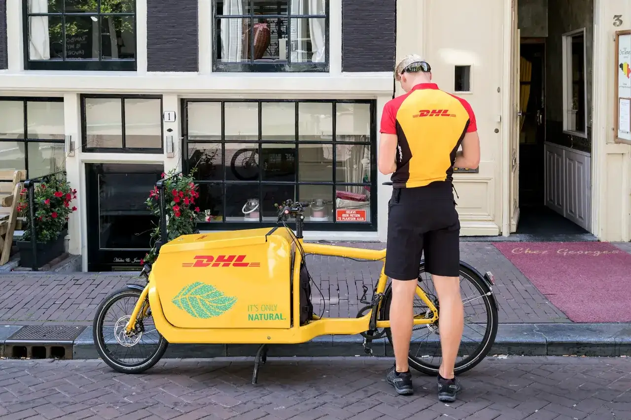 Kurier DHL z rowerem cargo na ulicy. Zastanawiasz się, ile idzie list z Polski do Holandii? Ten rower może pomóc w dostawie!