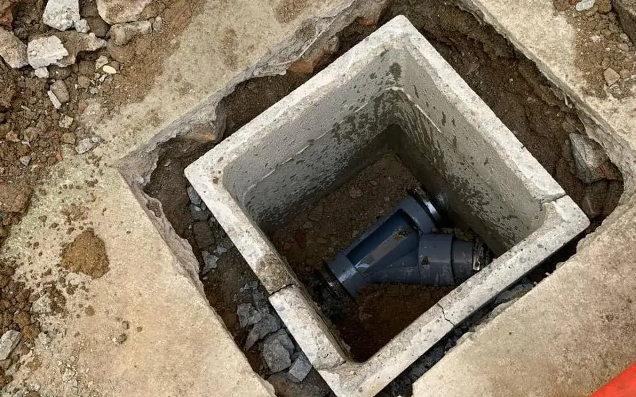 Un regard tout &agrave; l'&eacute;gout en b&eacute;ton, avec des tuyaux gris &agrave; l'int&eacute;rieur, entour&eacute; de terre et de gravats.