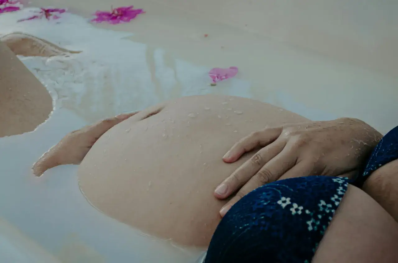 En gravid mage vilar i ett bad med blommor. En lugn stund för den som är basta gravid.