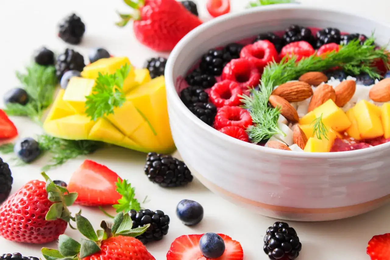 Kolorowa miska pełna owoców: maliny, jeżyny, borówki, mango, migdały. Niska zawartość indeksu glikemicznego wiśni sprawia, że to idealny wybór na zdrowy posiłek.