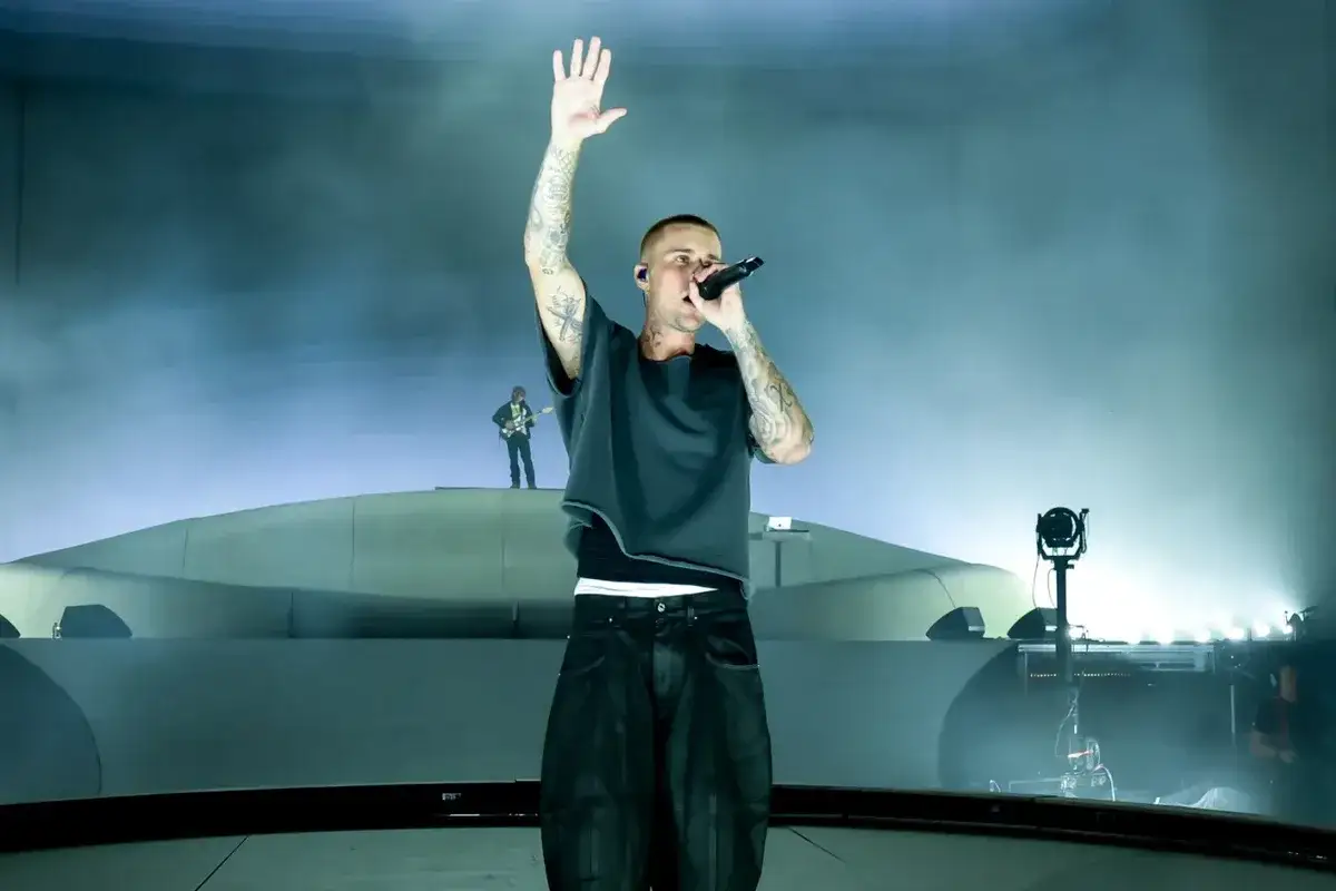 Justin Bieber w wieku dorosłym, z podniesioną ręką, śpiewa na scenie.