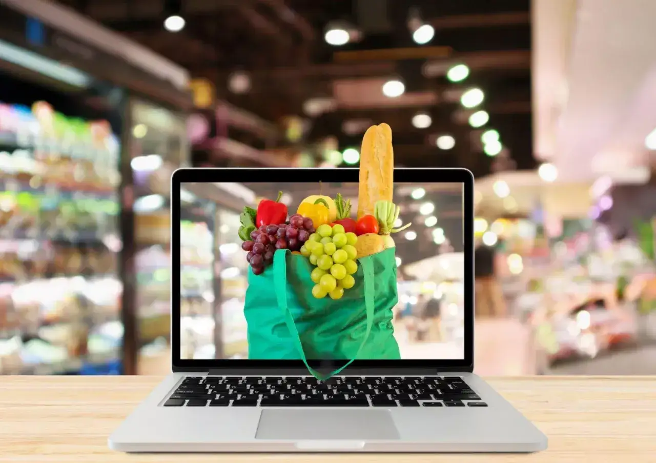 Laptop z ekranem pokazującym torbę pełną świeżych owoców i warzyw. To jest właśnie retail w nowoczesnym wydaniu – zakupy spożywcze online.