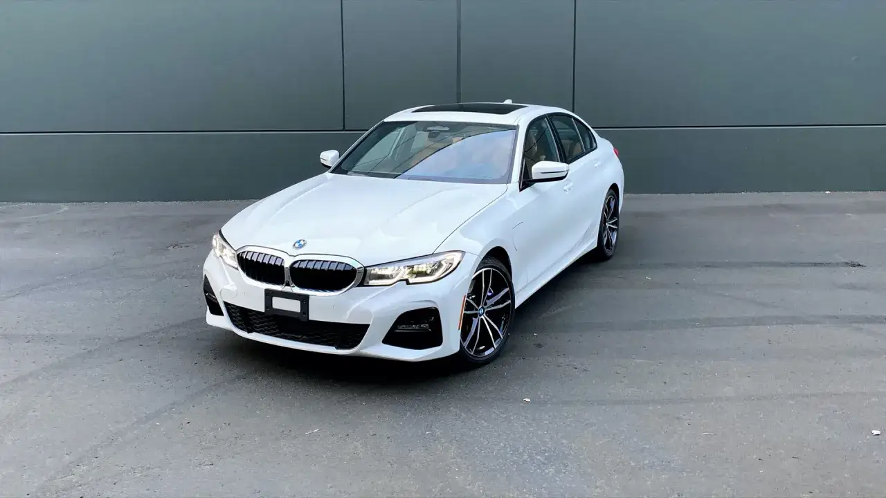 Białe BMW 330e z czarnym dachem i felgami stoi na tle szarej ściany.
