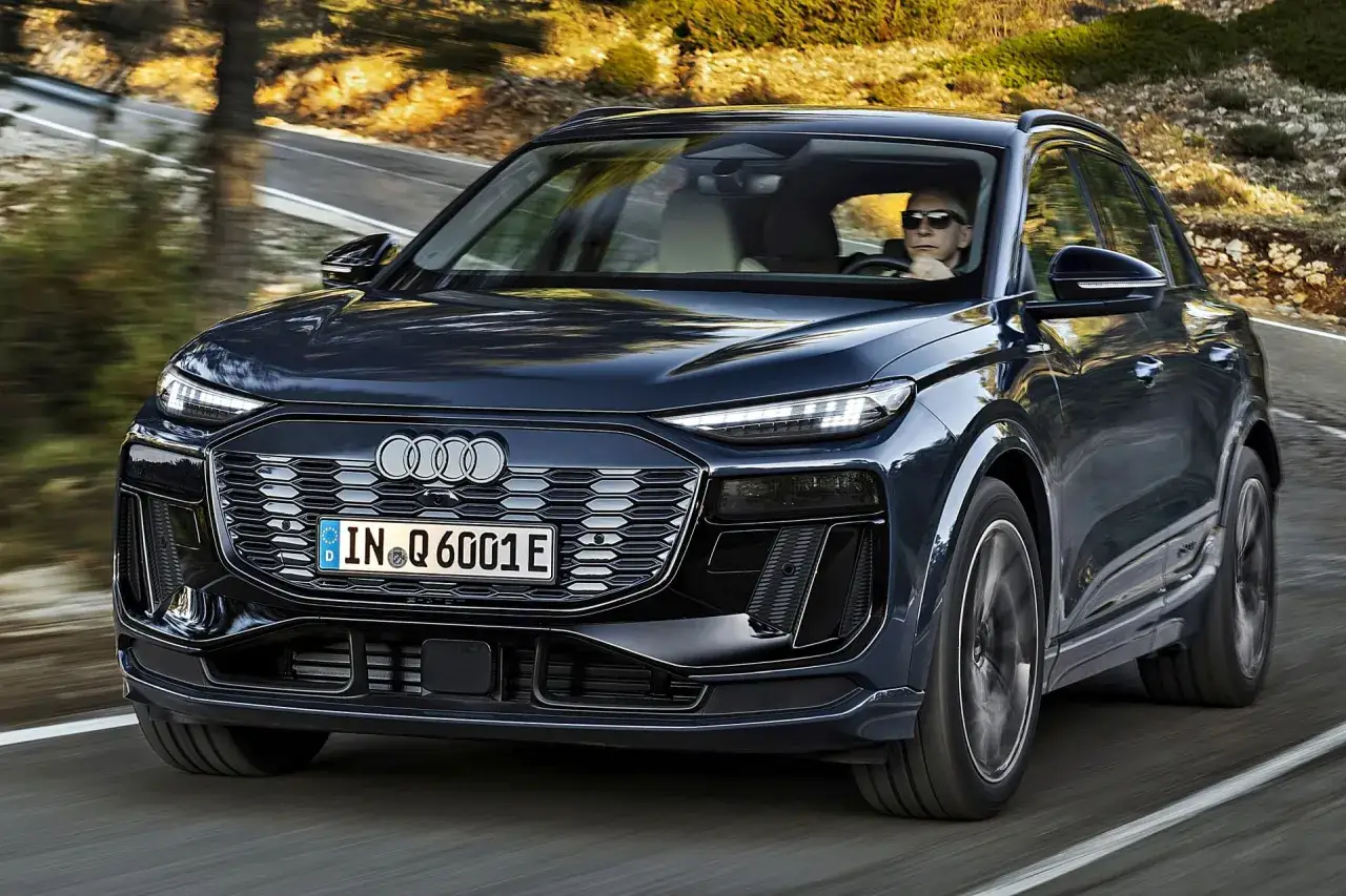 Ciemnogranatowy Audi Q6 e-tron jedzie po krętej drodze. Sprawdź aktualną audi q6 e-tron cenę.
