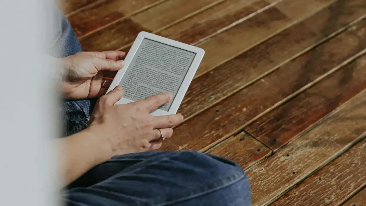 Une personne lit sur une tablette encre &eacute;lectronique, assise sur un plancher en bois.