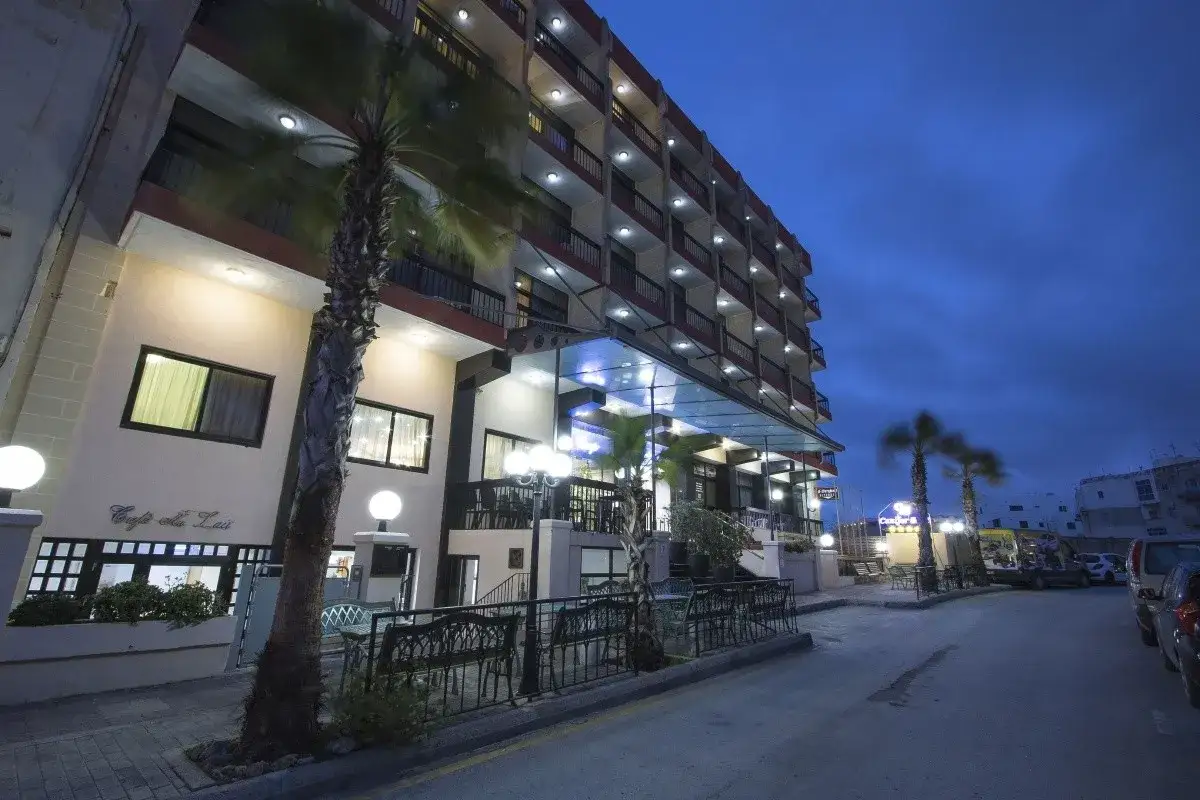 Hotel Canifor Malta nocą, z palmami i oświetlonym budynkiem.