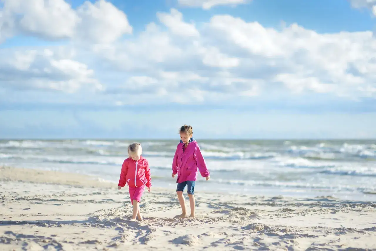 Zwei M&auml;dchen in pinken Jacken erkunden den Strand. Perfekte Urlaubziele mit Kindern f&uuml;r unvergessliche Momente am Meer.