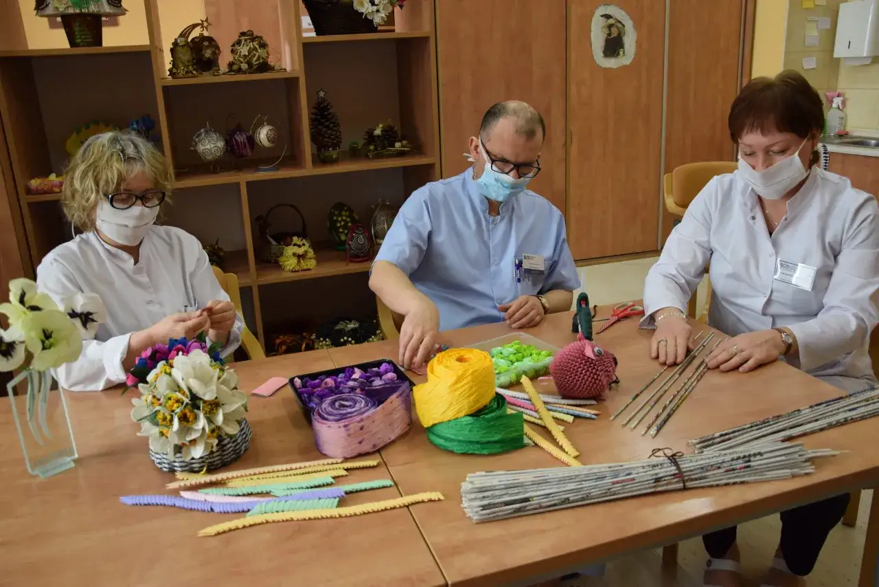 Terapeuta zajęciowy z zespołem tworzy ozdoby z papieru i materiał&oacute;w.