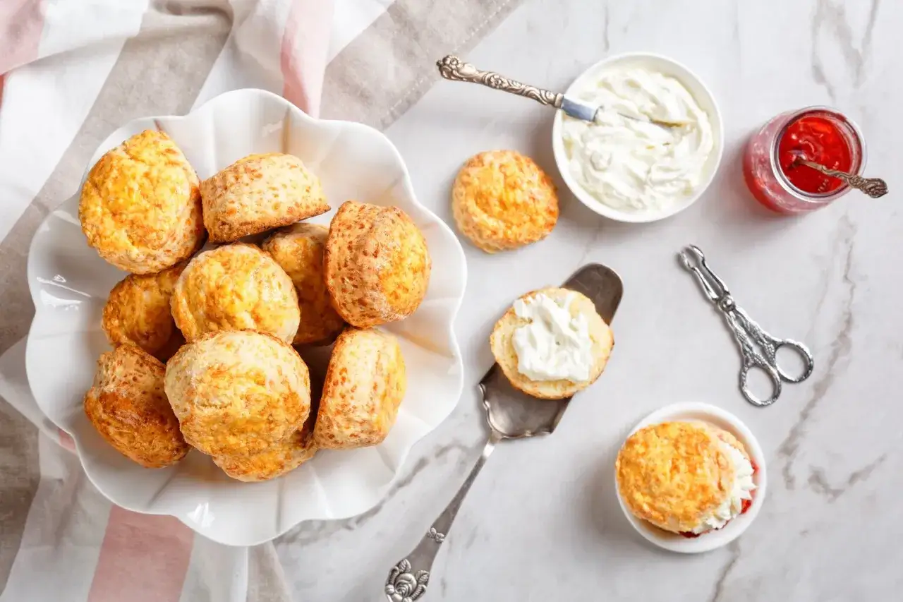 En skål med gyllene engelska scones, serverade med vispad grädde och jordgubbssylt. Perfekt för en mysig fika.