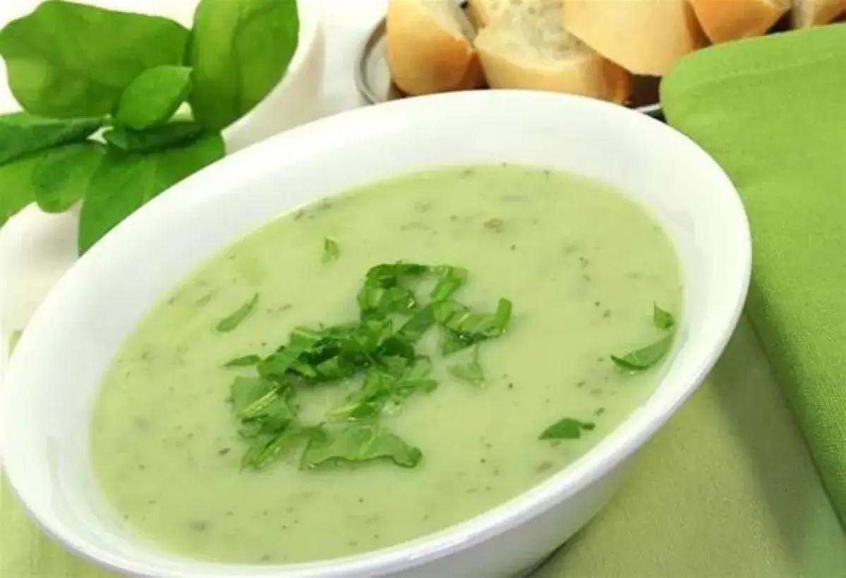Un bol de soupe &agrave; l'oseille cr&eacute;meuse, garnie d'herbes fra&icirc;ches, avec du pain et une serviette verte en arri&egrave;re-plan.