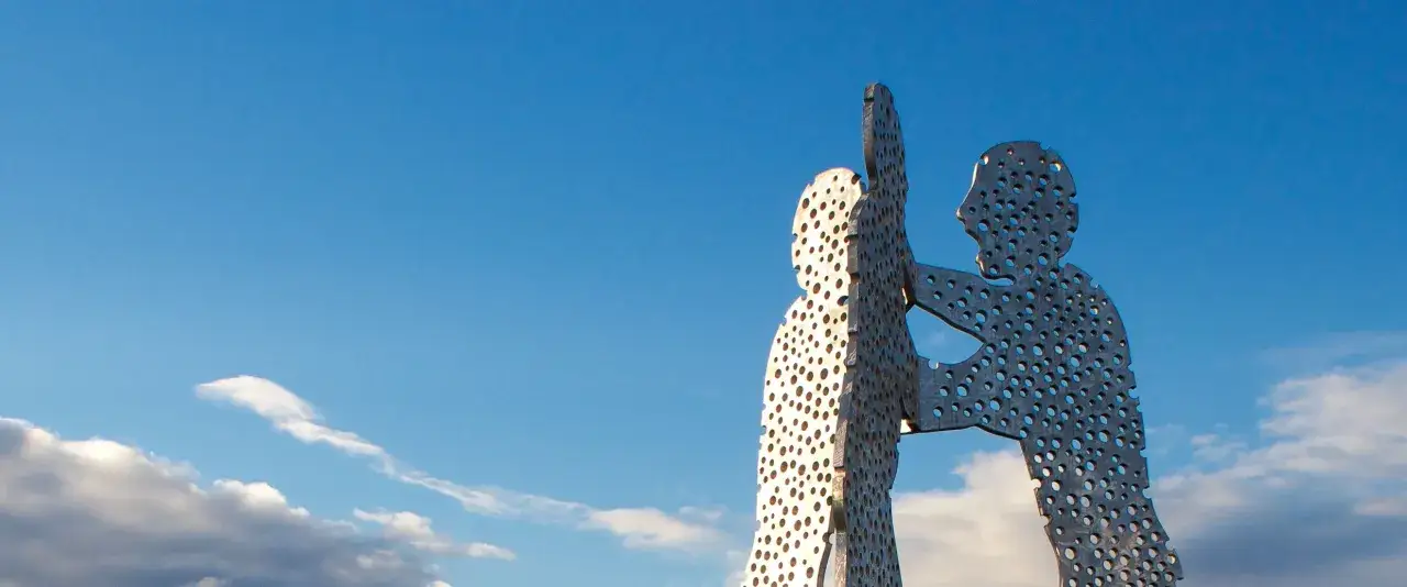 Der Molecule Man Berlin, eine Skulptur aus Metall mit vielen Löchern, ragt gegen einen blauen Himmel mit Wolken.