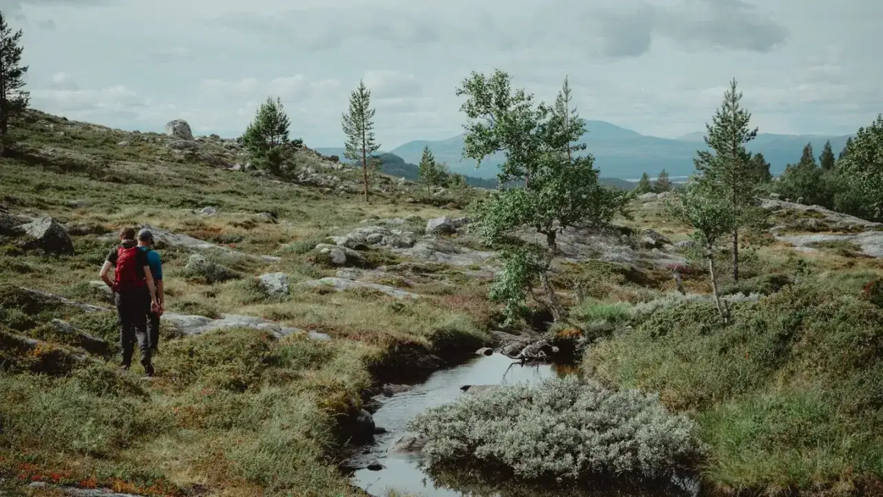 Två vandrare går genom ett stenigt landskap med en bäck. Kanske är det deras första camp Mellsta.