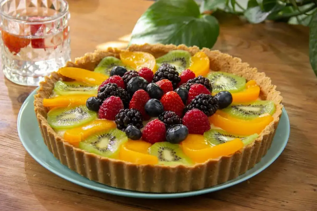 Tarta de frutas fresca y colorida, con kiwi, melocotón, frambuesas, moras y arándanos, lista para disfrutar.