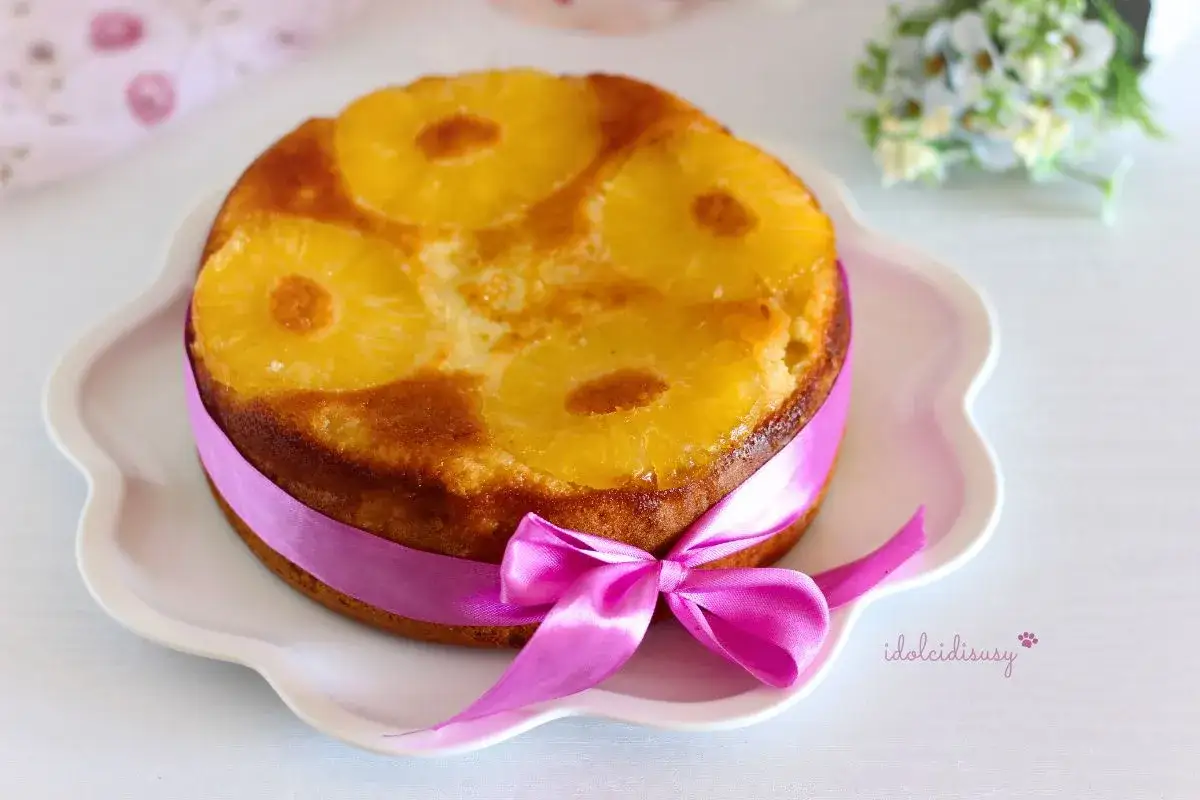Torta ananas capovolta, decorata con un nastro rosa e un fiocco, pronta per essere gustata.