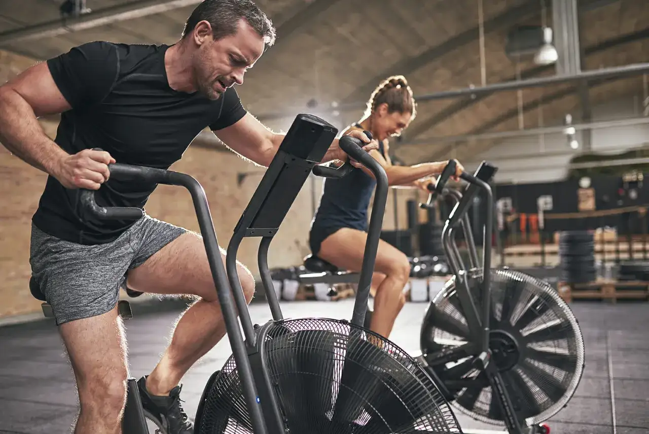 Un homme et une femme s'entraînent intensément sur des vélos d'air, un entraînement cardio exigeant.