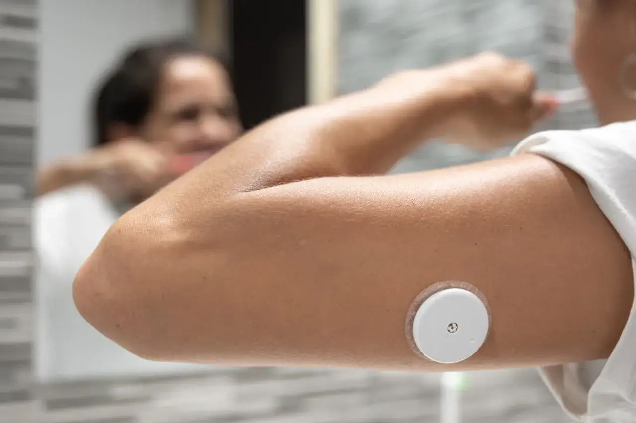 Eine Person mit einem Glukosesensor am Arm putzt sich die Z&auml;hne. Dies hilft bei der &Uuml;berwachung von zuckerkrankheiten.