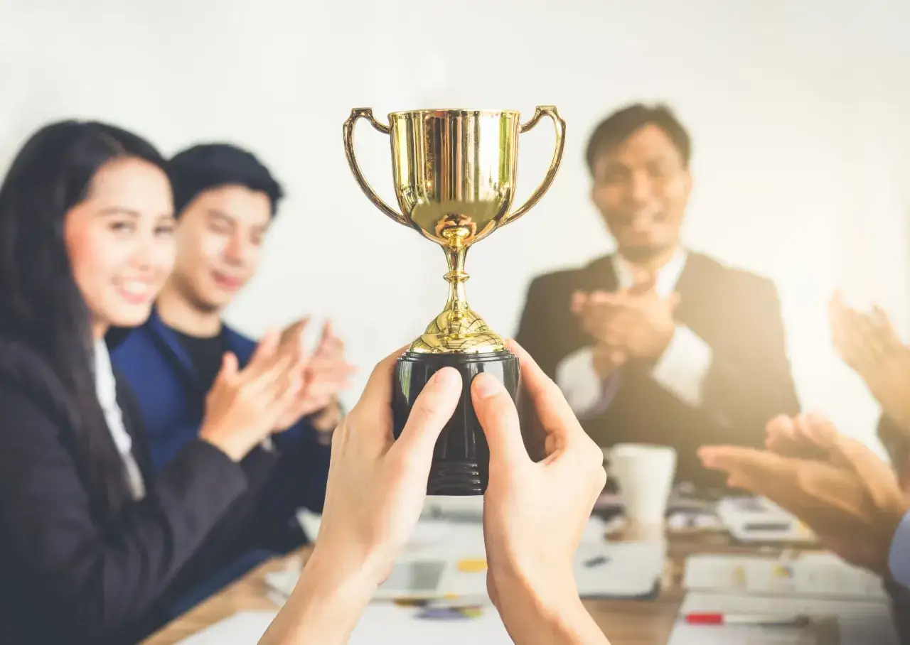 Hands hold a golden trophy, symbolizing award recognition ideas. A smiling team applauds in the background.