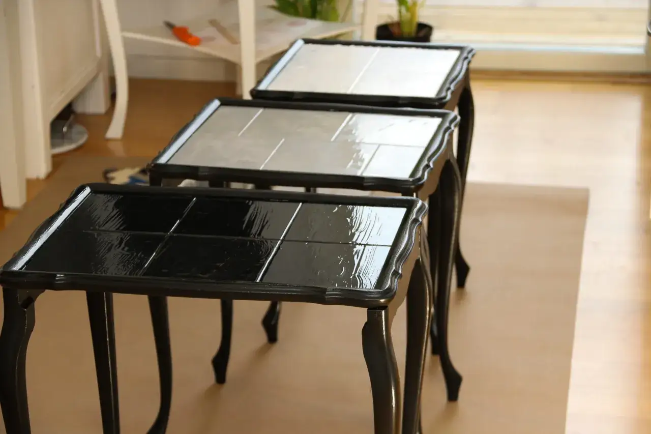 Tre små bord med svarta, blanka toppar som nyligen målats. Ett projekt för att måla ekbord svart.