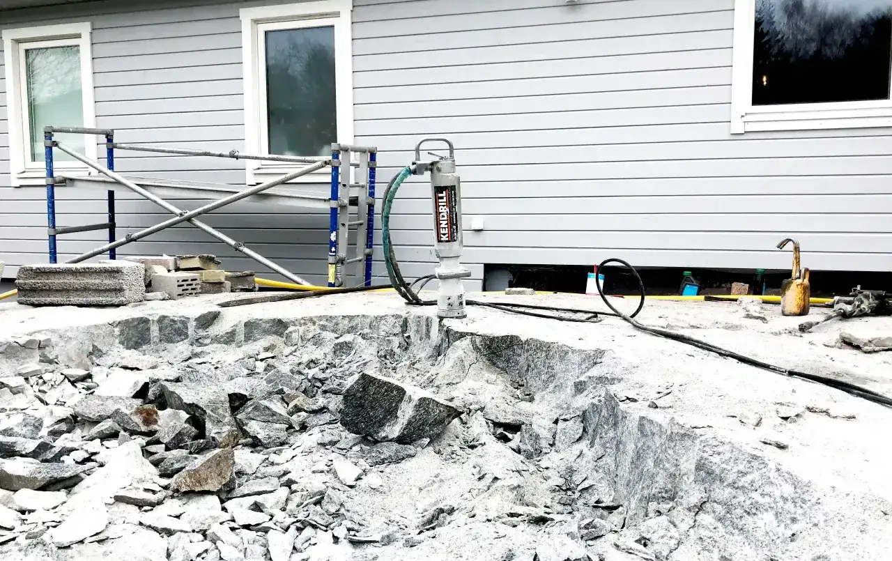 En borrmaskin är igång och förbereder för att borra i sten vid ett husbygge.