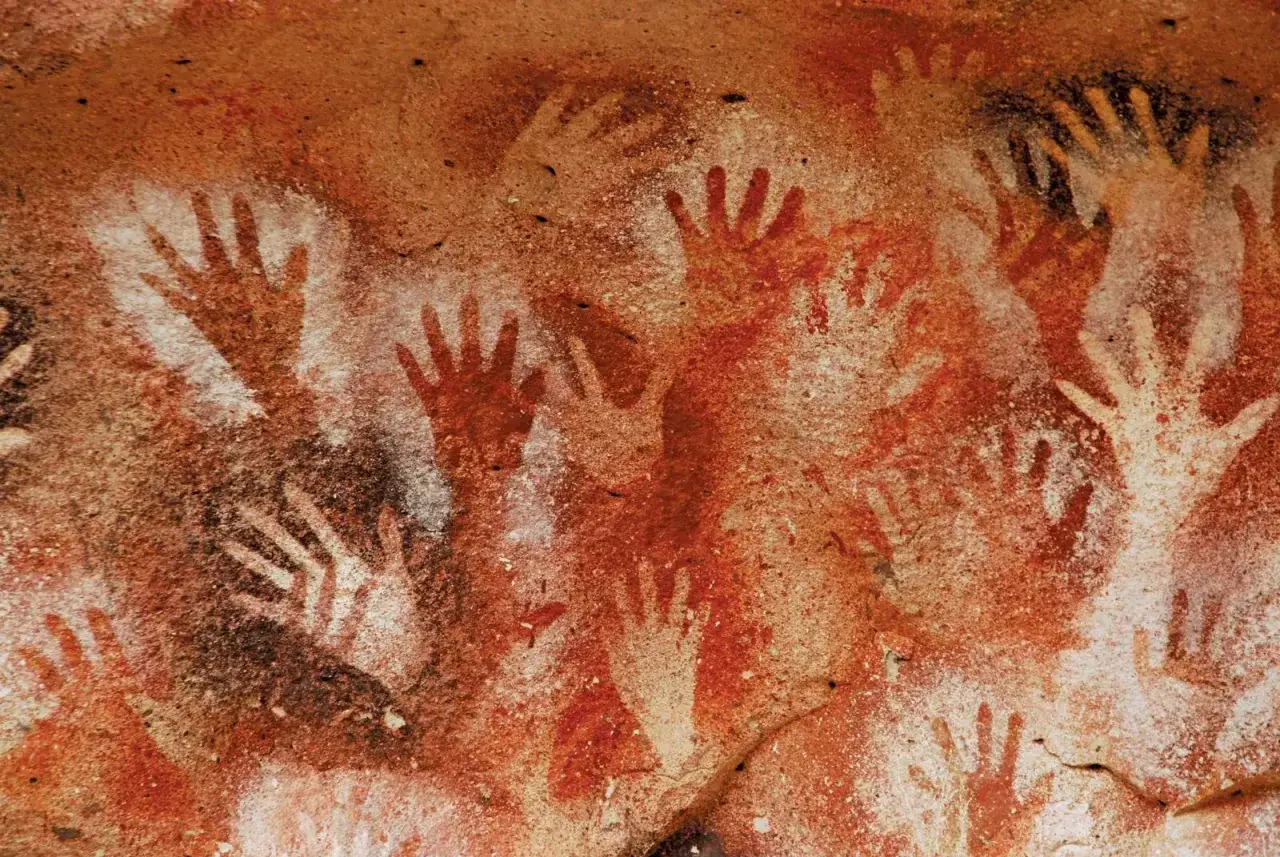 Många handavtryck i rött och vitt på en grottvägg, liknande de i Lascaux.