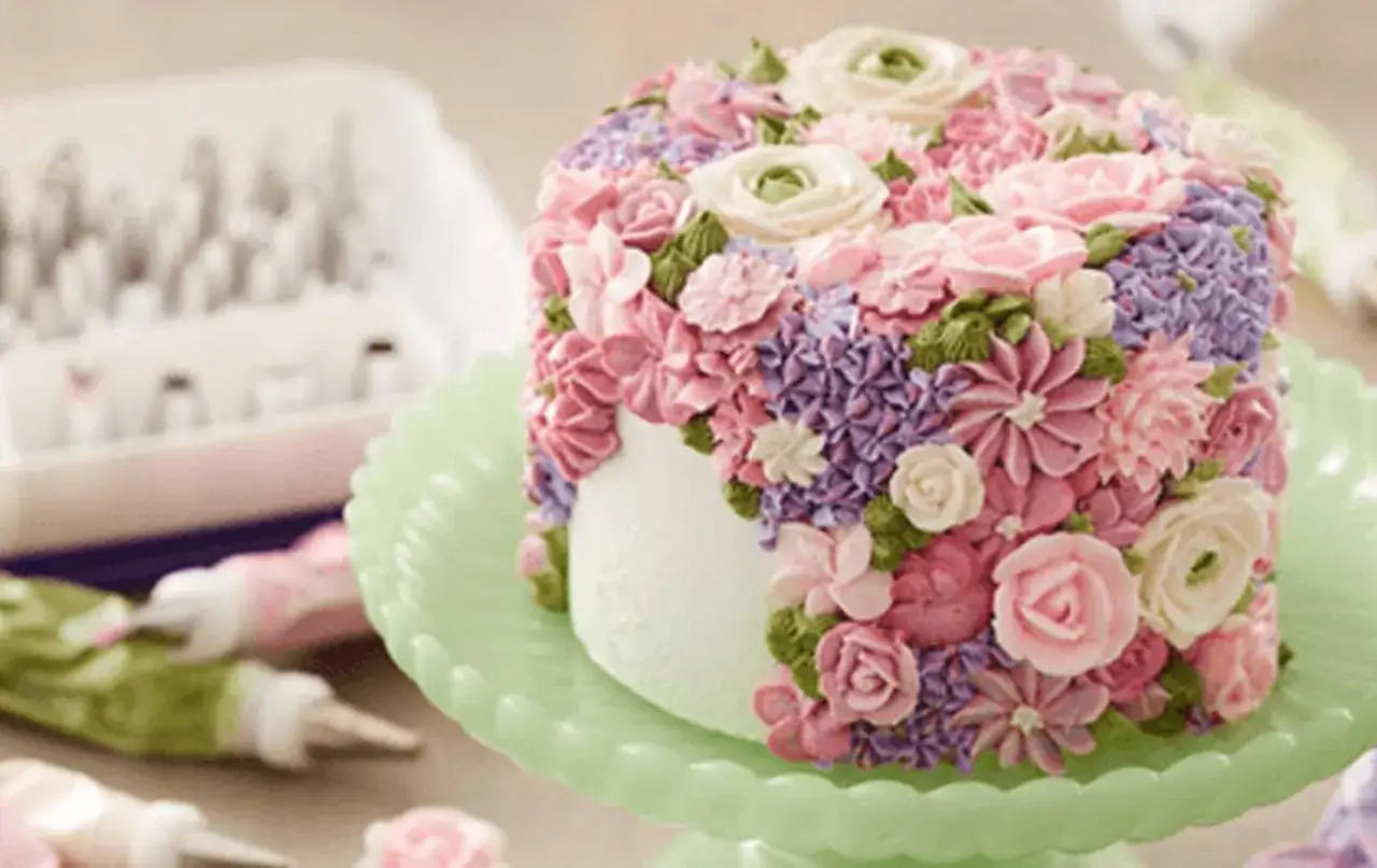 En tårta täckt av vackra blommor skapade med spritsa tårta med frosting i rosa, lila och gröna nyanser.