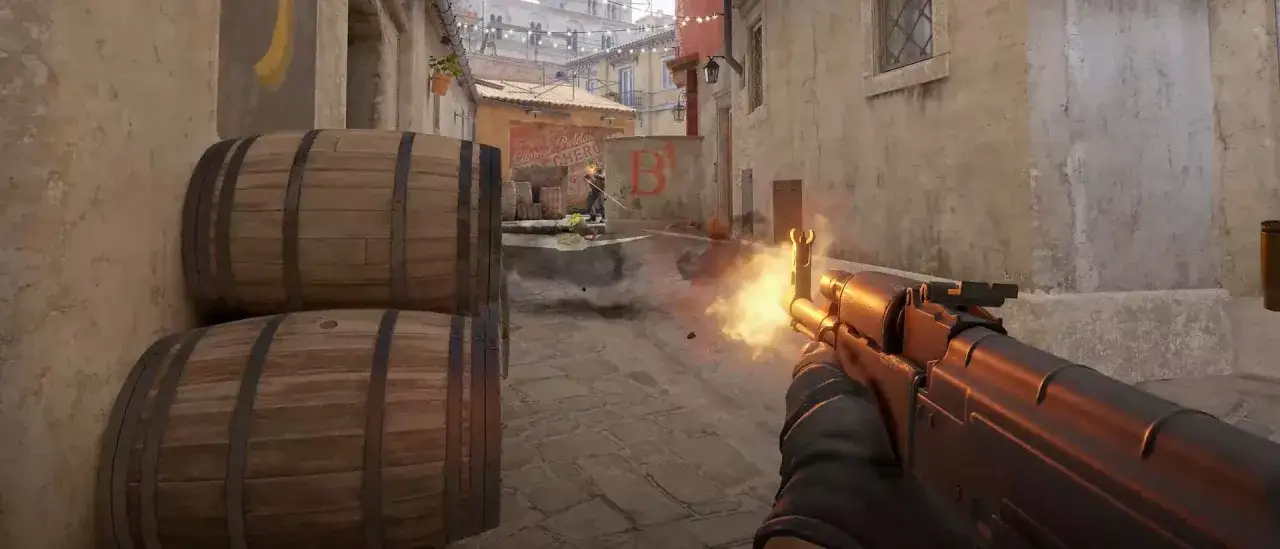Gracz w Counter-Strike 2 strzela z karabinu, wybuchają płomienie. W tle beczki i wąska uliczka.