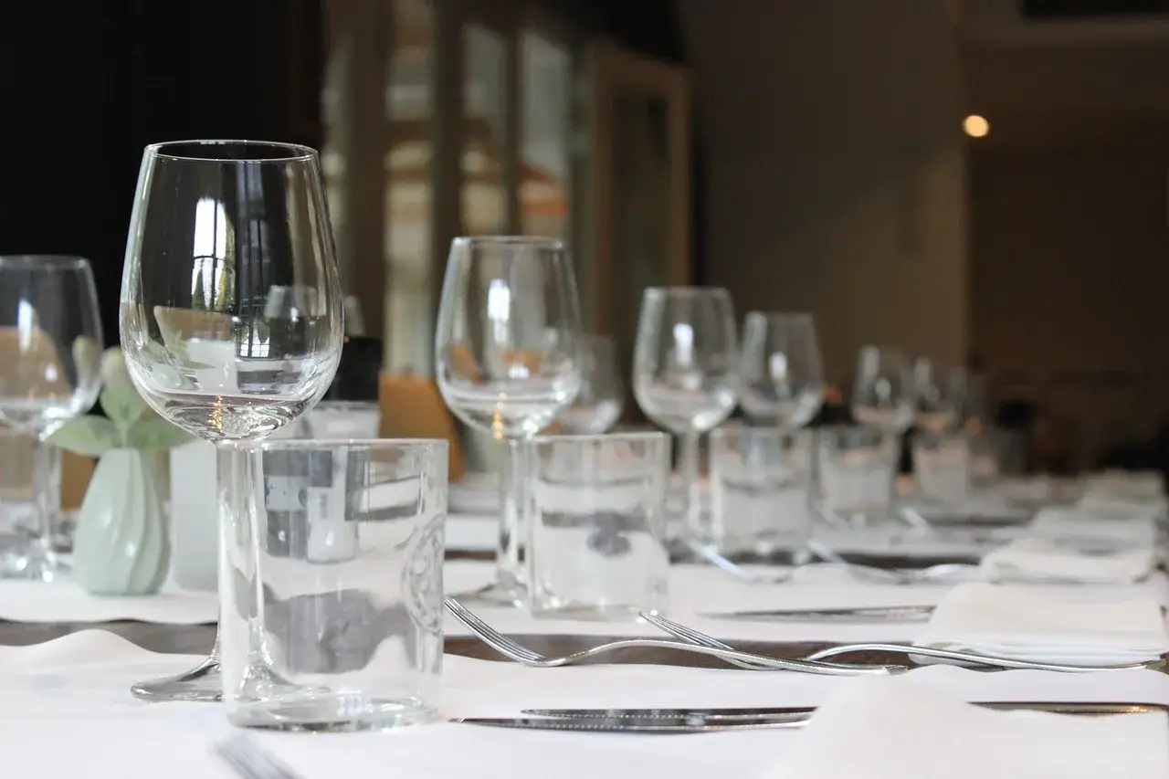 Un verre à eau à gauche, devant une table dressée pour un repas.