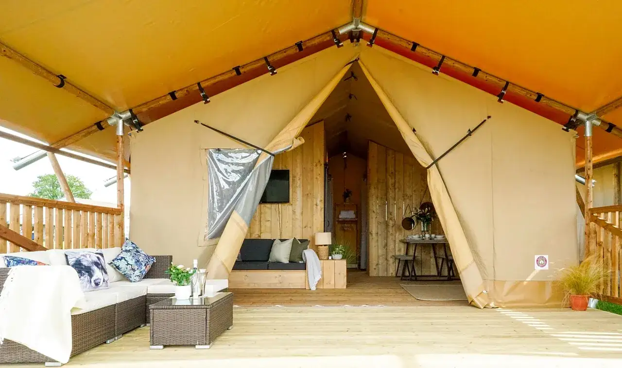 Luksusowy namiot safari, czyli glamping co to jest: wygodna sofa, stolik kawowy, jadalnia i taras.