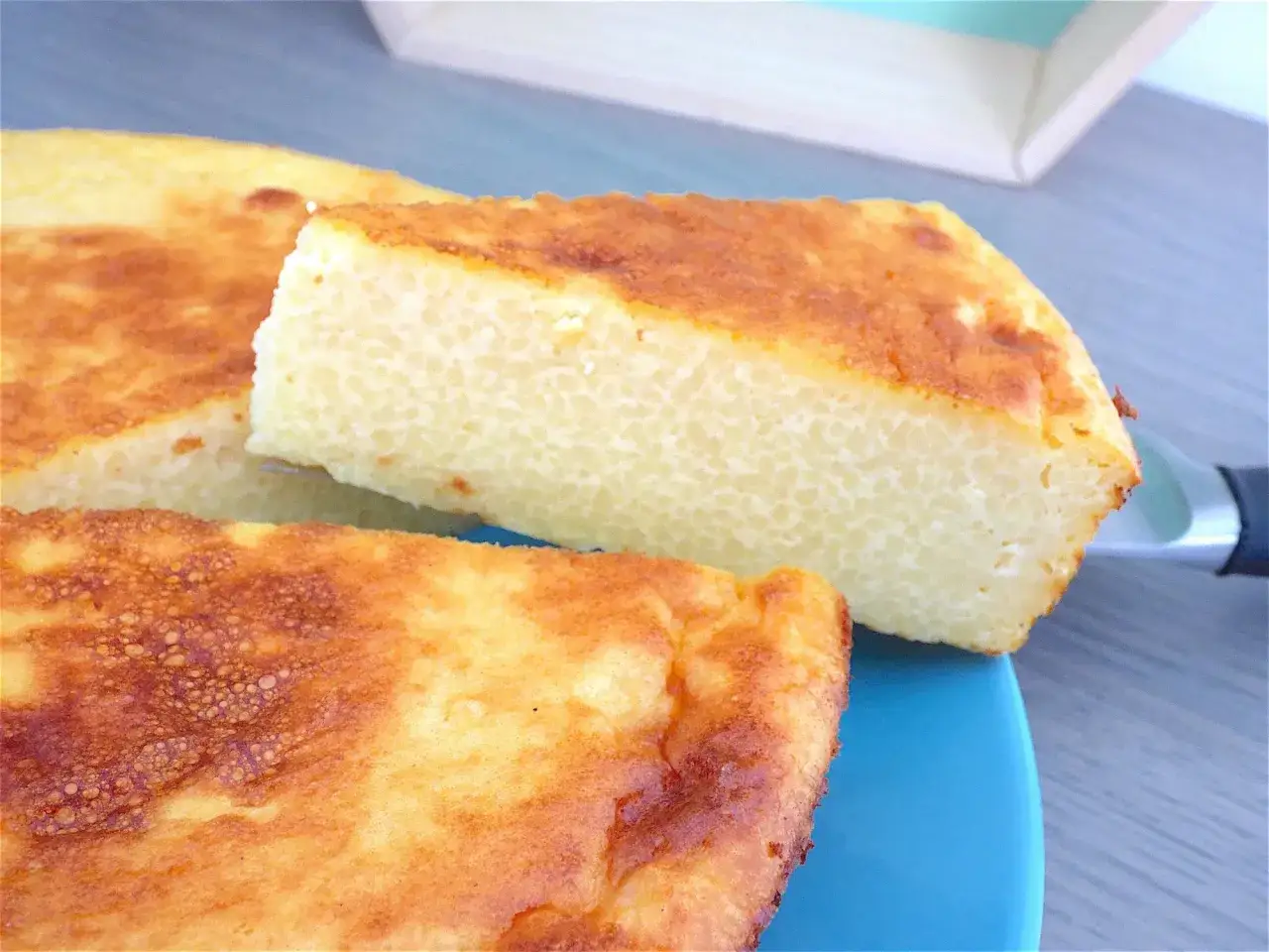 G&acirc;teau dor&eacute; &agrave; la semoule, texture a&eacute;r&eacute;e. Une part est soulev&eacute;e par une fourchette, r&eacute;v&eacute;lant la diff&eacute;rence semoule et couscous.