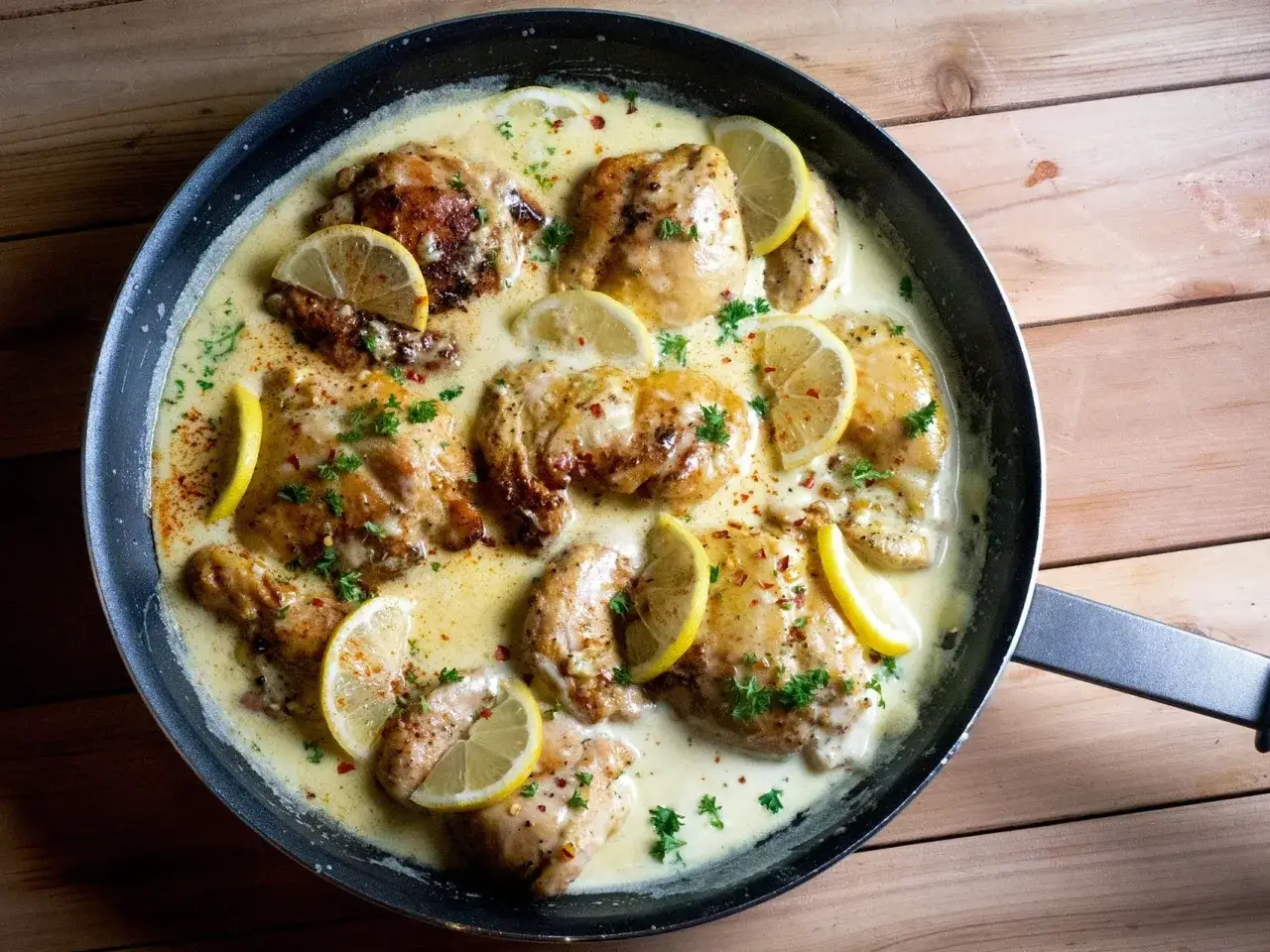 Succulento petto di pollo al limone in padella, guarnito con fette di limone fresco e prezzemolo tritato.