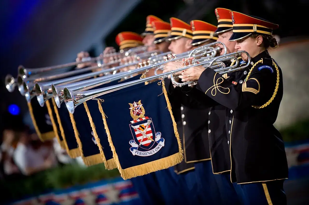 Orkiestra wojskowa grająca na trąbkach, słychać uroczystą fanfarę.