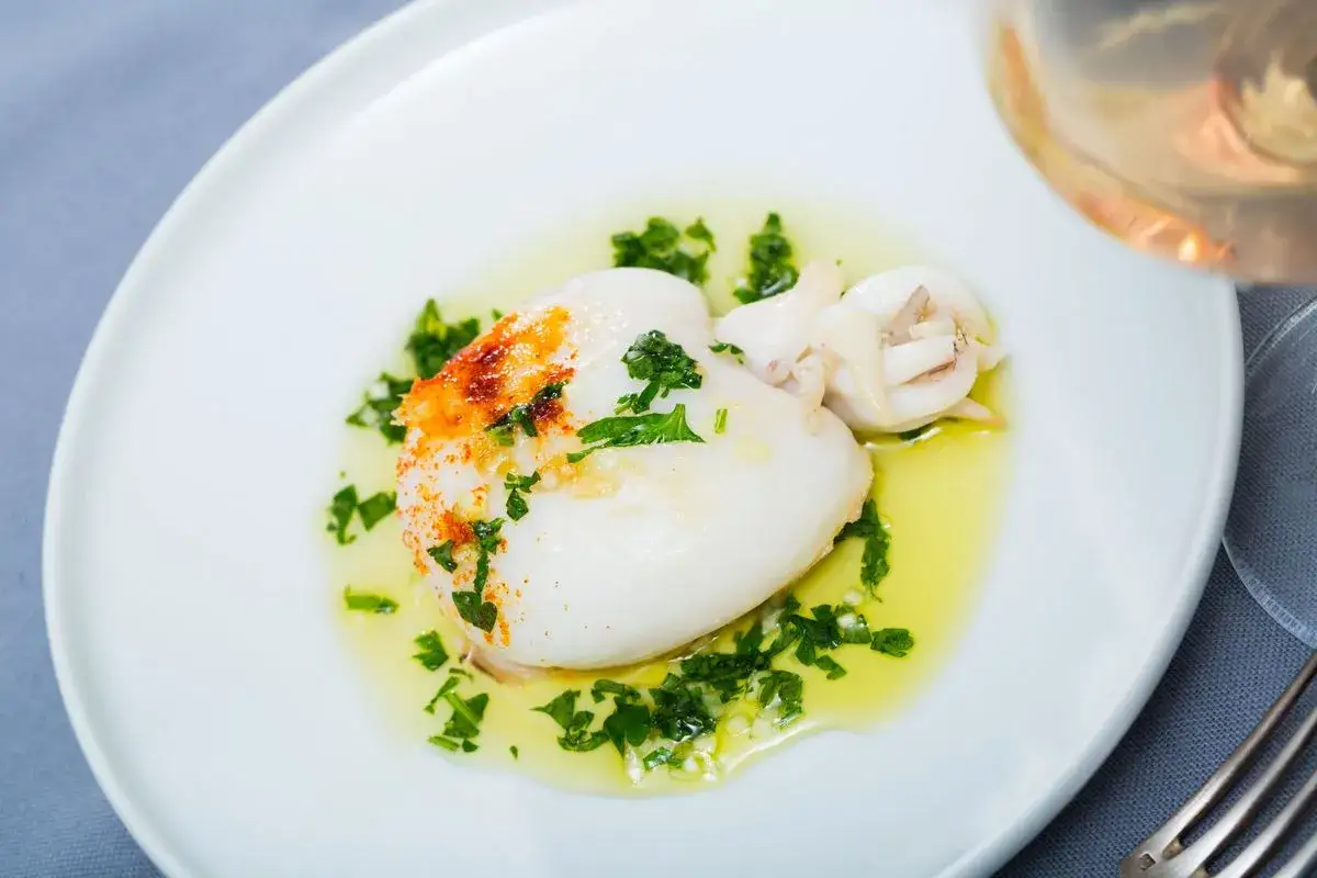 Jibia en salsa, tierna y jugosa, con perejil fresco y un toque de piment&oacute;n, servida en un plato blanco.