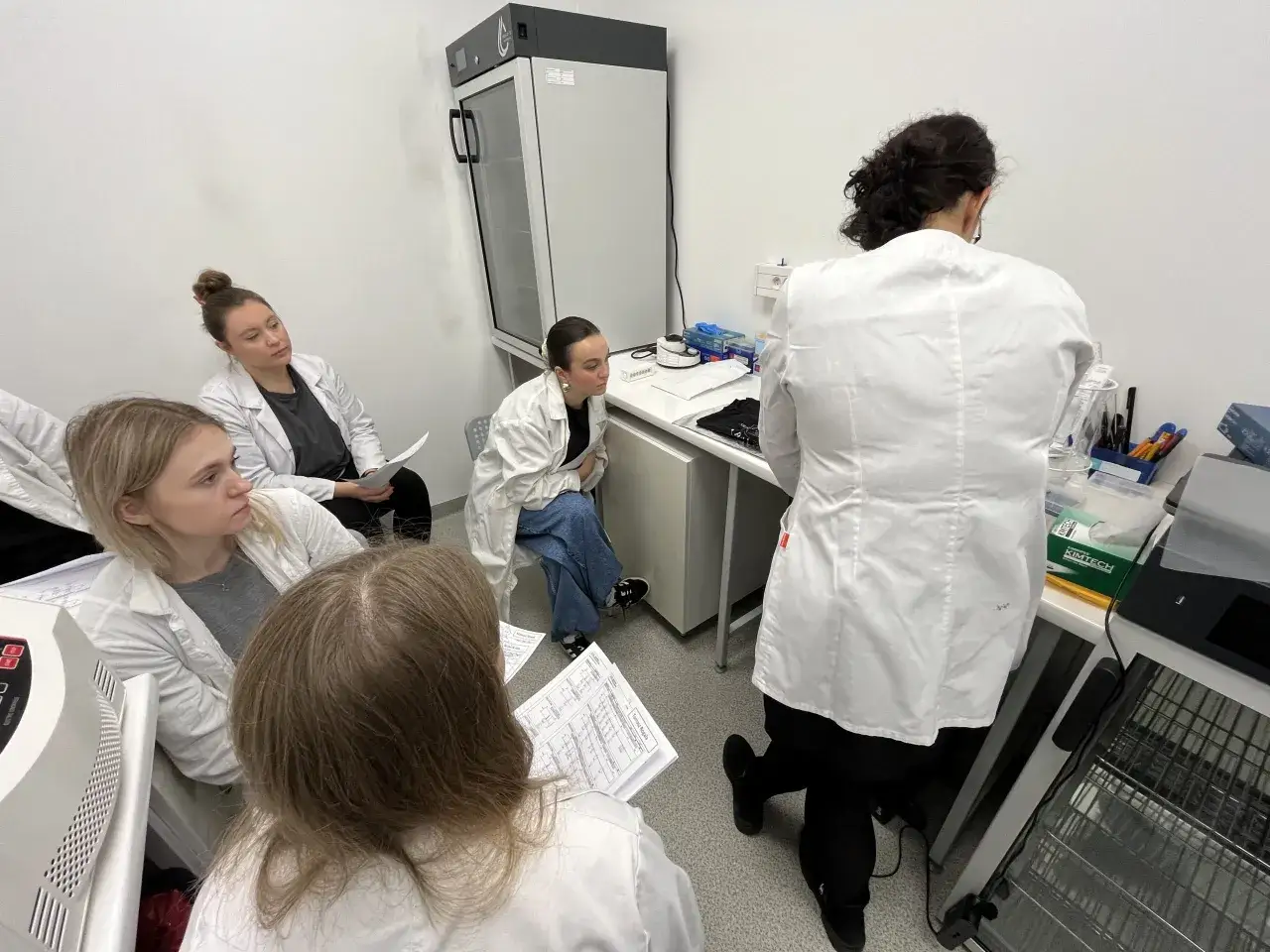 Grupa studentów w kitlach słucha wykładu w laboratorium. Czy praca w laboratorium jest trudna? Zależy od podejścia!