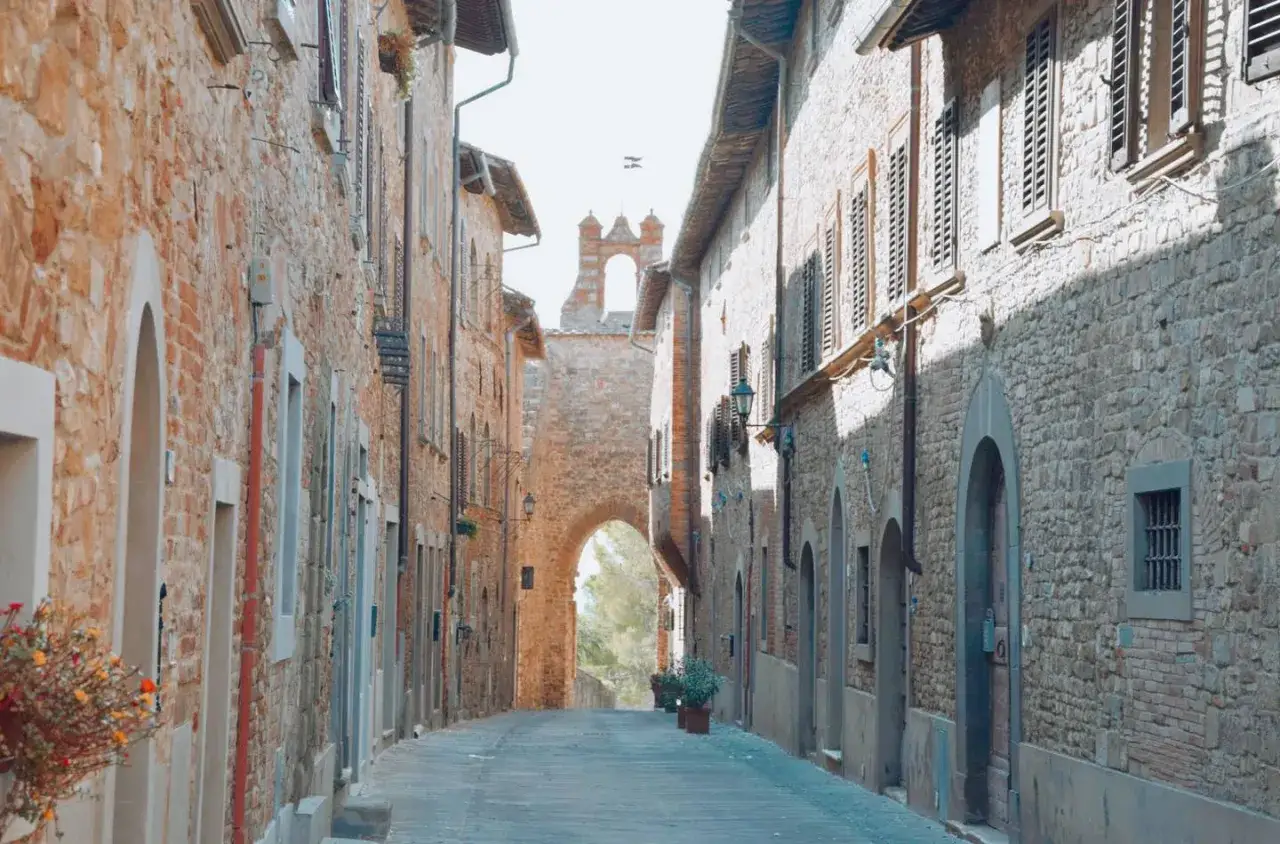 Un vicolo tra antichi borghi medievali vicino Firenze, con case in pietra e mattoni, un arco in fondo e un campanile.