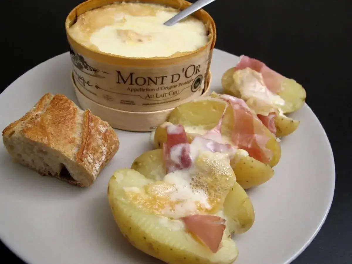 Un plat r&eacute;confortant de pommes de terre garnies de fromage fondu et de charcuterie, accompagn&eacute; d'une cro&ucirc;te de pain.